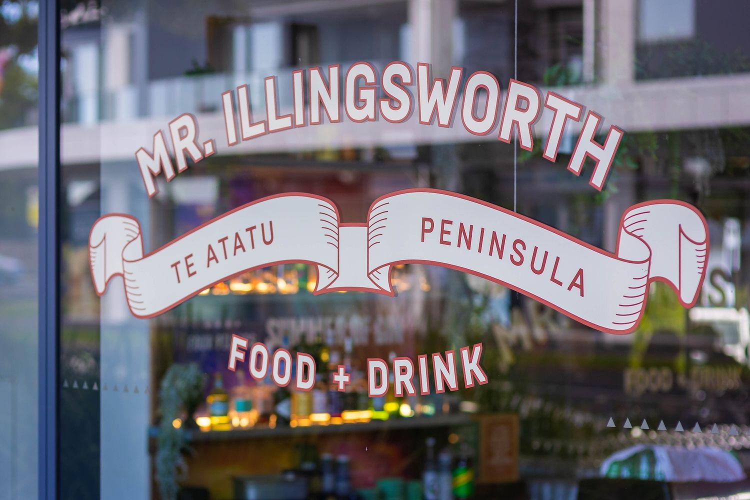 Illuminated storefront signs for food and drink establishments with 'Te Atatu Peninsula' text visible at night.