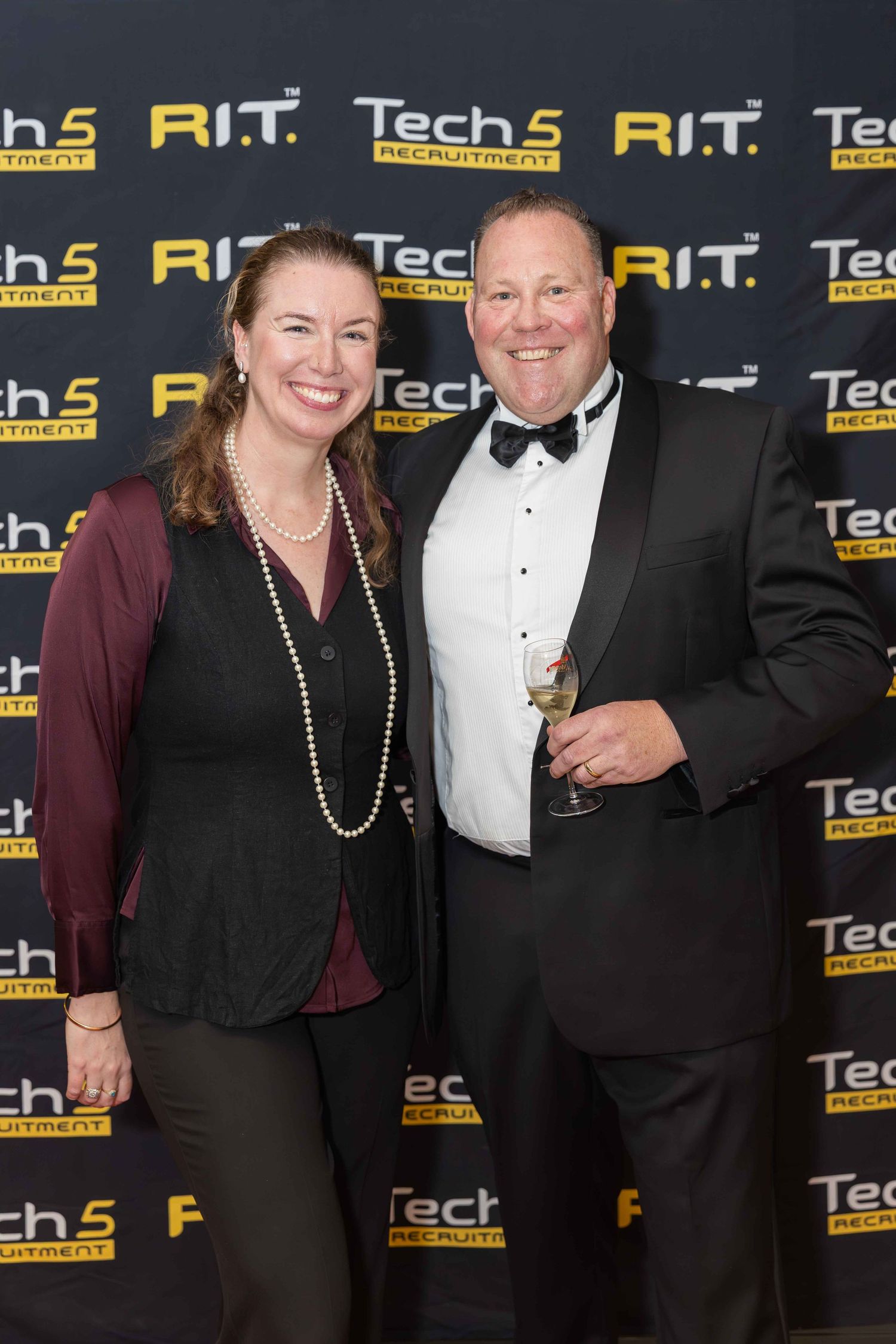 A smiling man and woman pose at a Tech5 Recruitment event, dressed in formal attire against a branded backdrop.