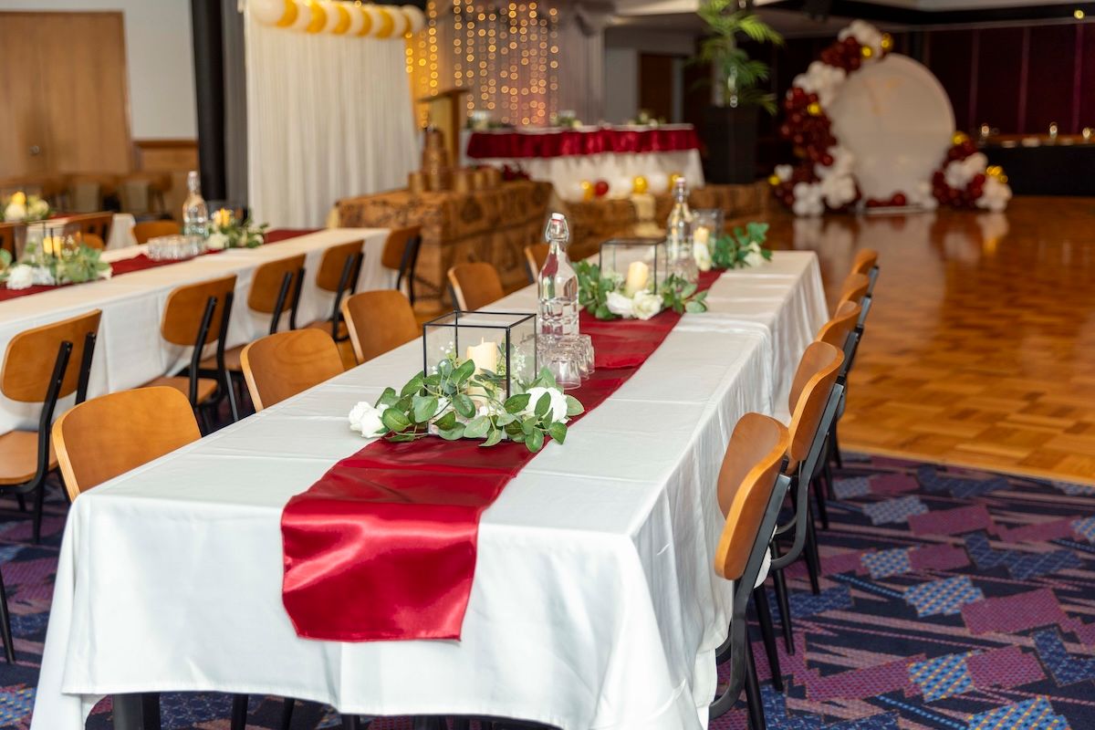 Elegant banquet hall setup with white tablecloths, burgundy accents, and crystal chandeliers for a formal event.