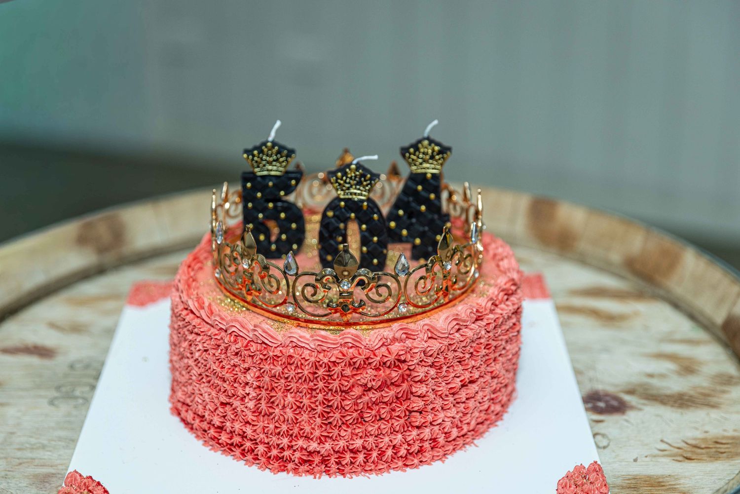Pink rosette birthday cake with gold crown and black number 30 candles on a rustic wooden table.