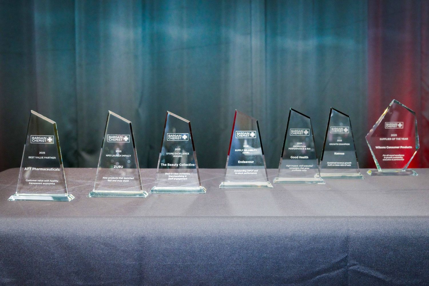 Row of glass or crystal award trophies displayed on dark surface.
