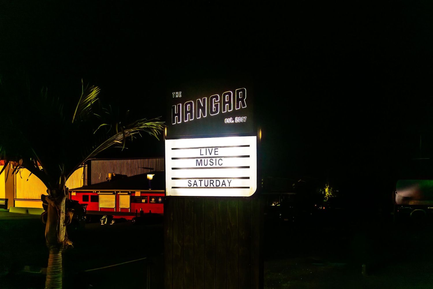 Illuminated storefront signs glow against the dark night sky in a strip mall setting.