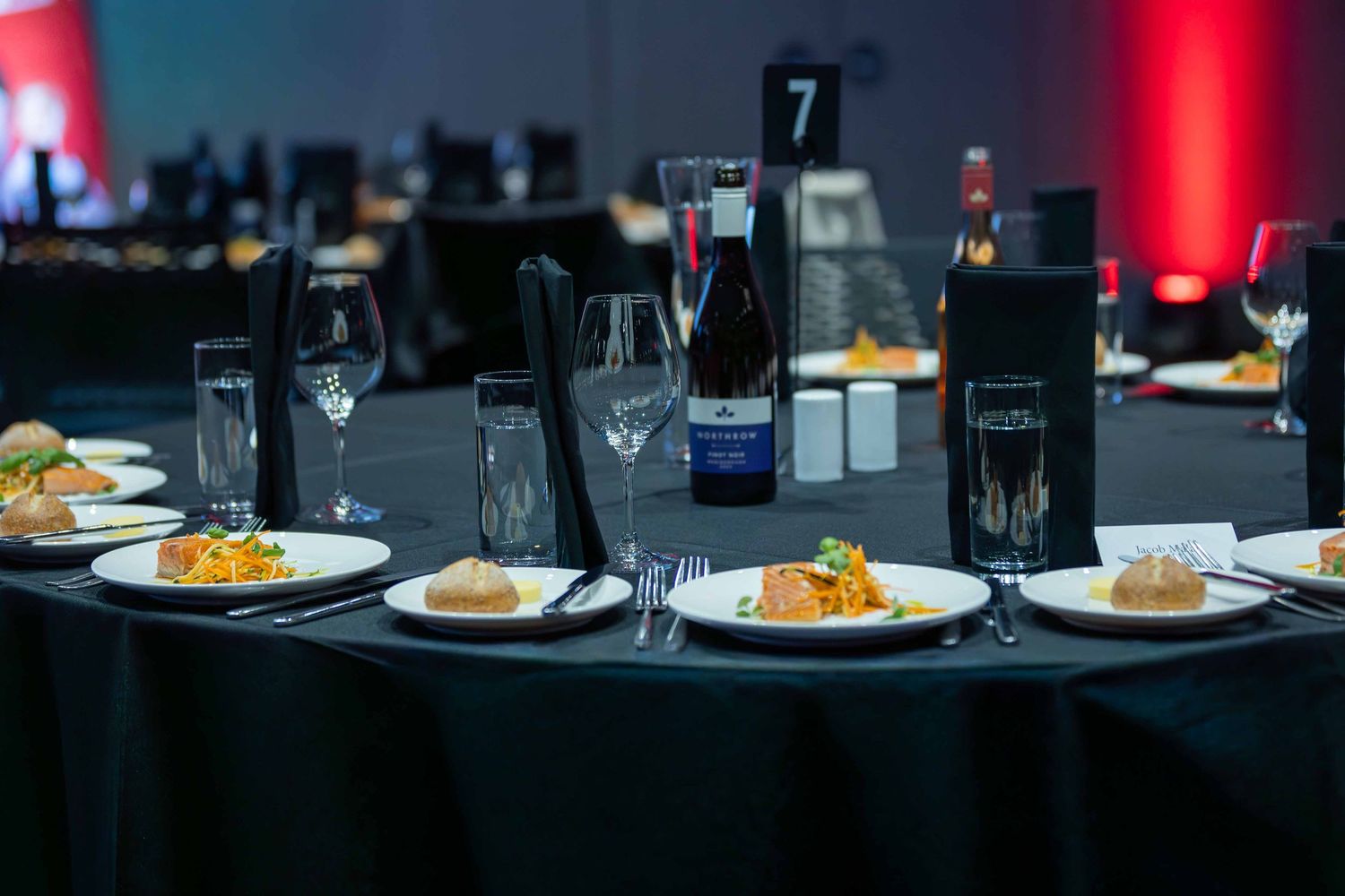 Formal dinner setup with plated meals and wine glasses on dark tables.