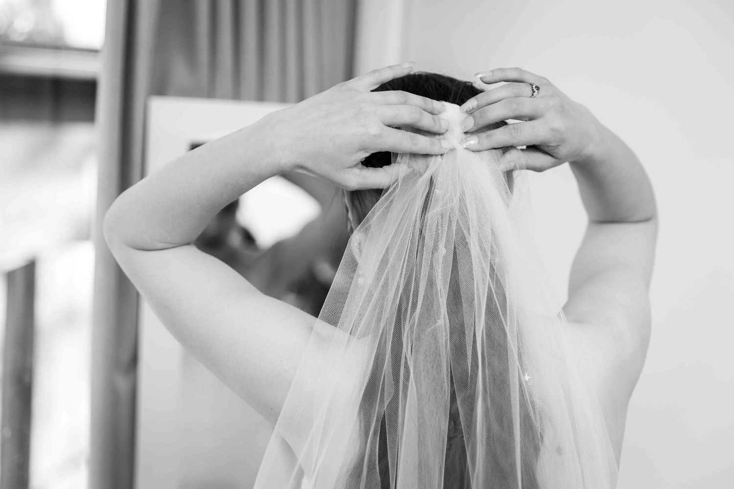 Bride adjusting her wedding veil in black and white photo, elegant bridal preparation moment.