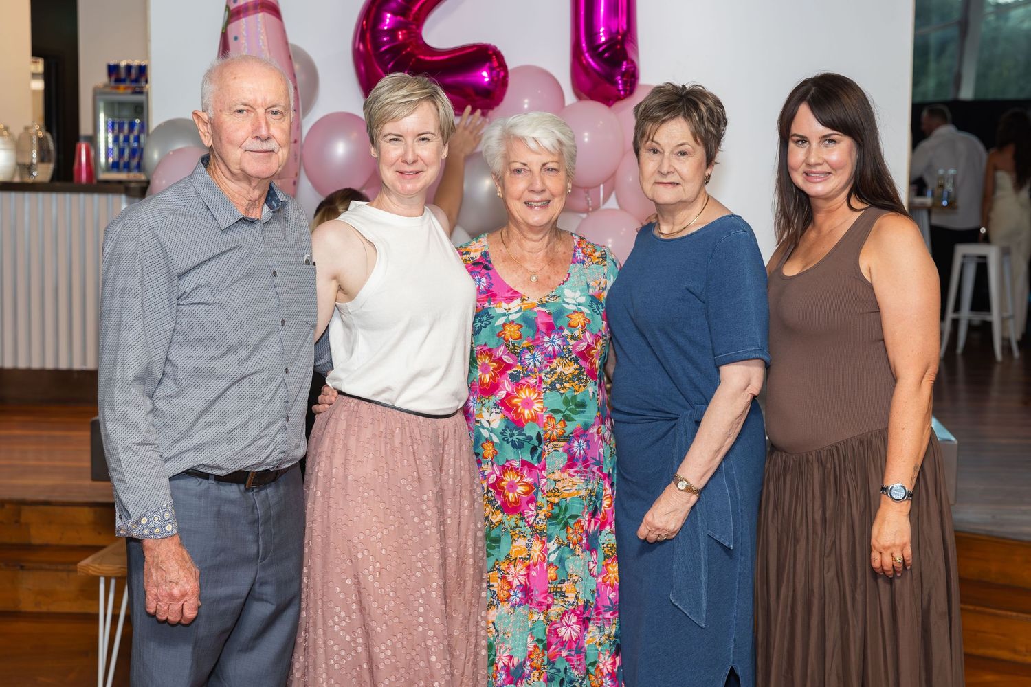 Five adults smiling together at a 21st birthday party celebration with pink balloons and decorations in the background.