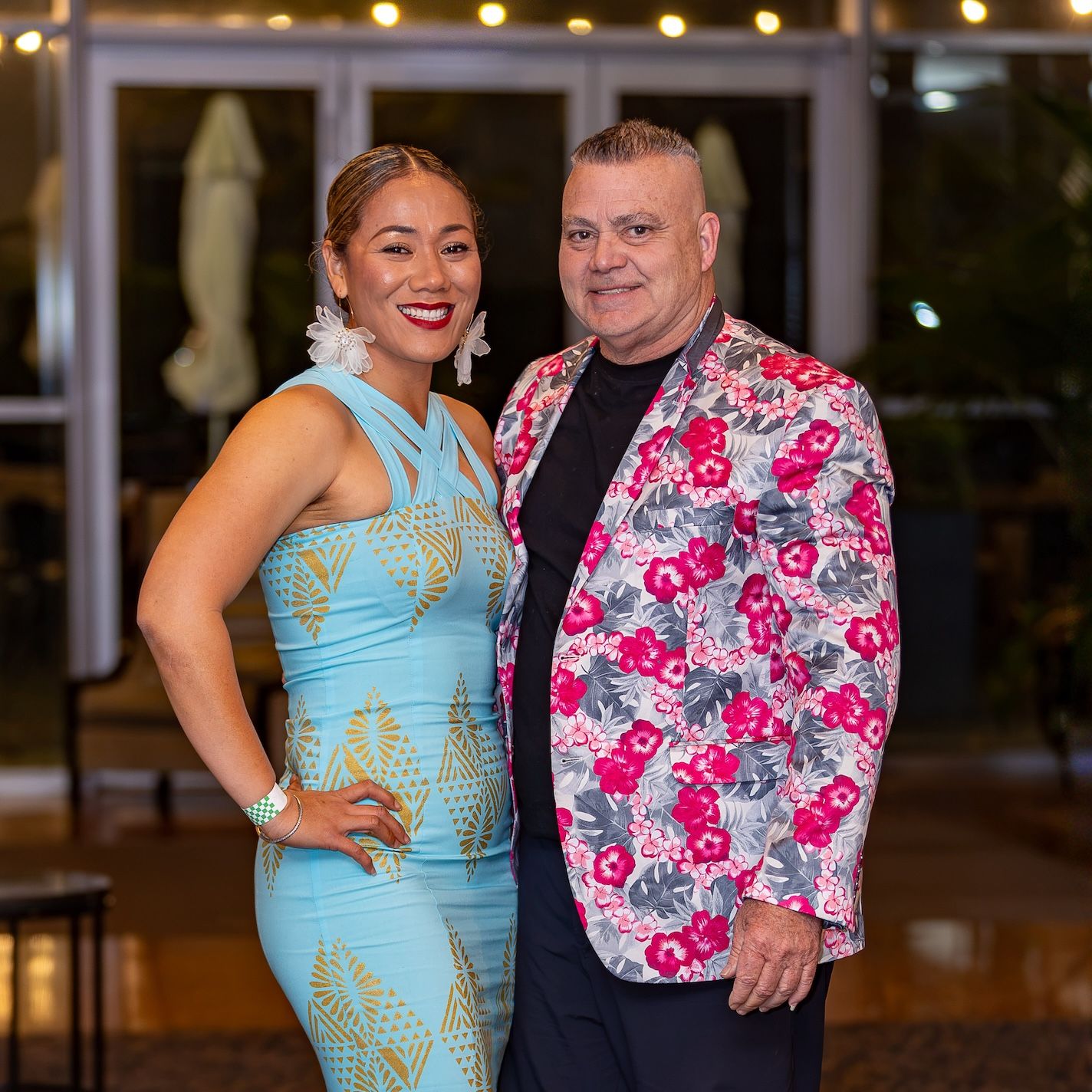 Couple posing elegantly, woman in light blue dress and man in floral blazer, at a formal evening event.