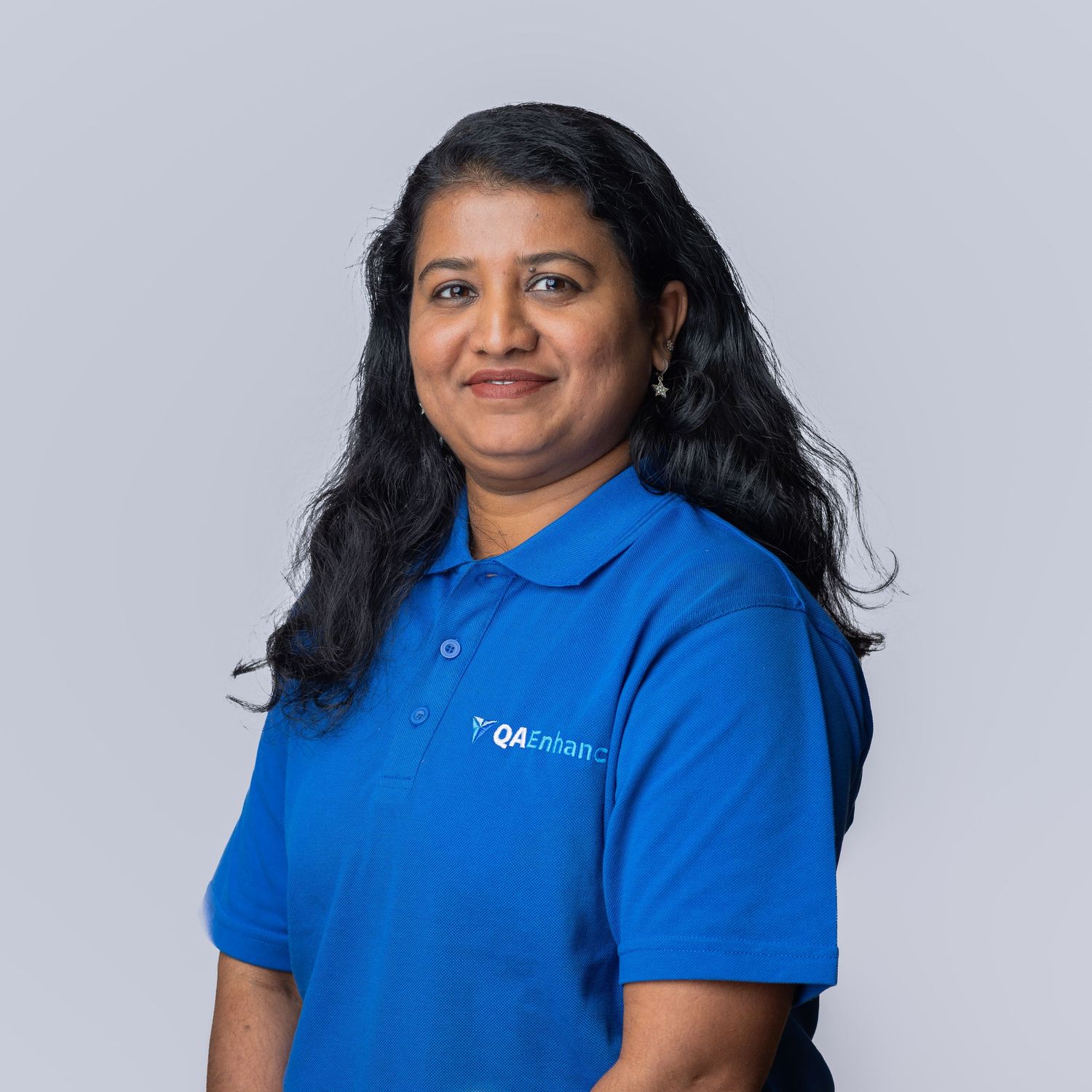 Woman in blue QADean polo shirt smiling against gray background, professional corporate headshot portrait.