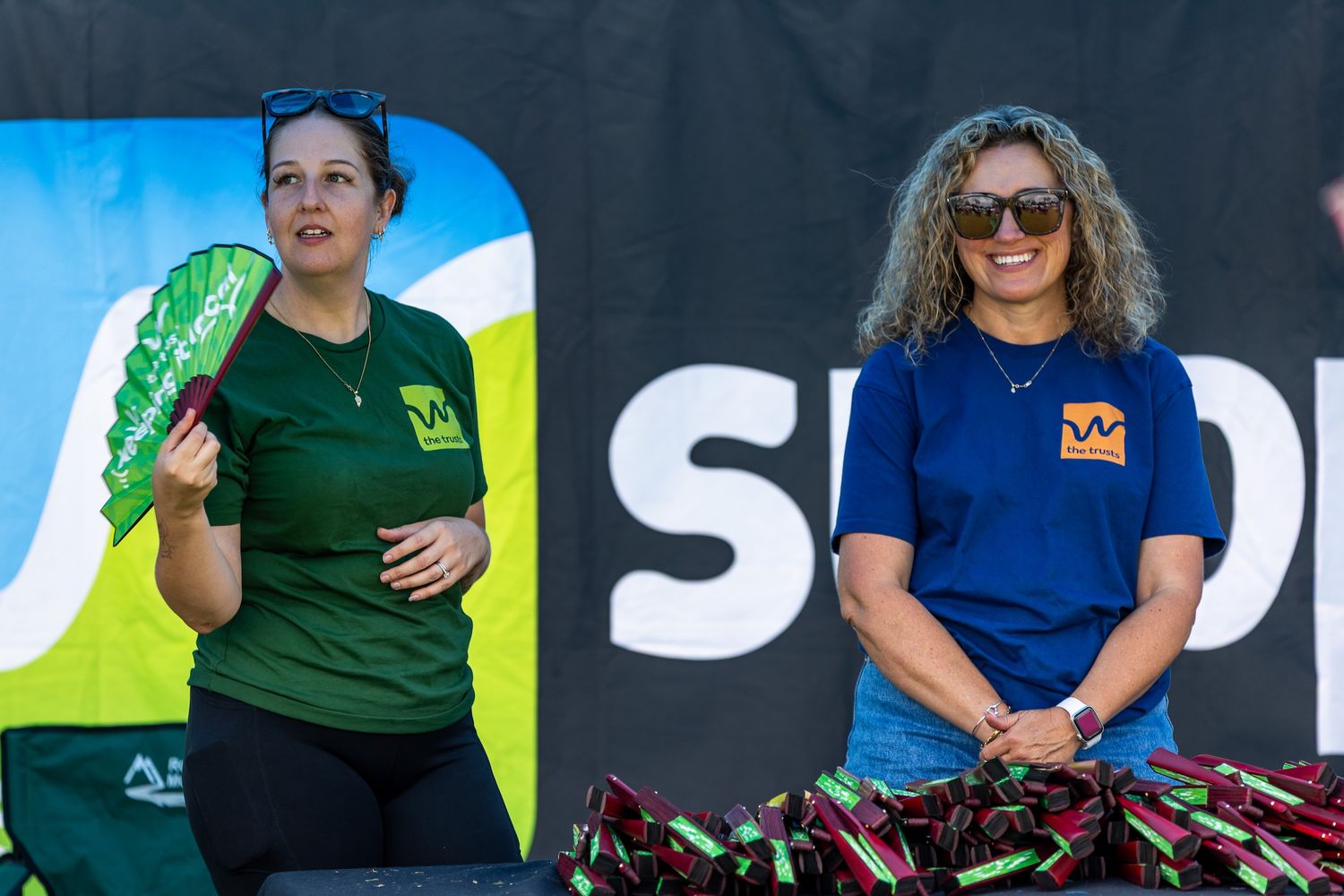 Event staff in blue and green shirts working at an outdoor festival booth.