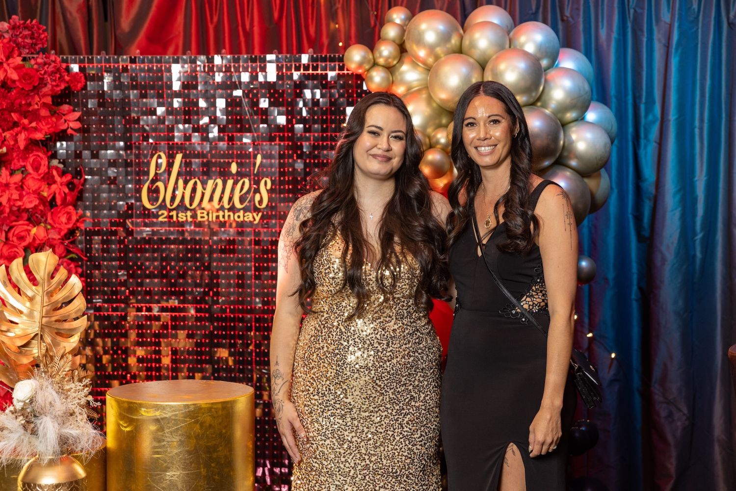 Two women posing at Ebonie's 21st birthday party in front of a sequin backdrop with balloon arch.