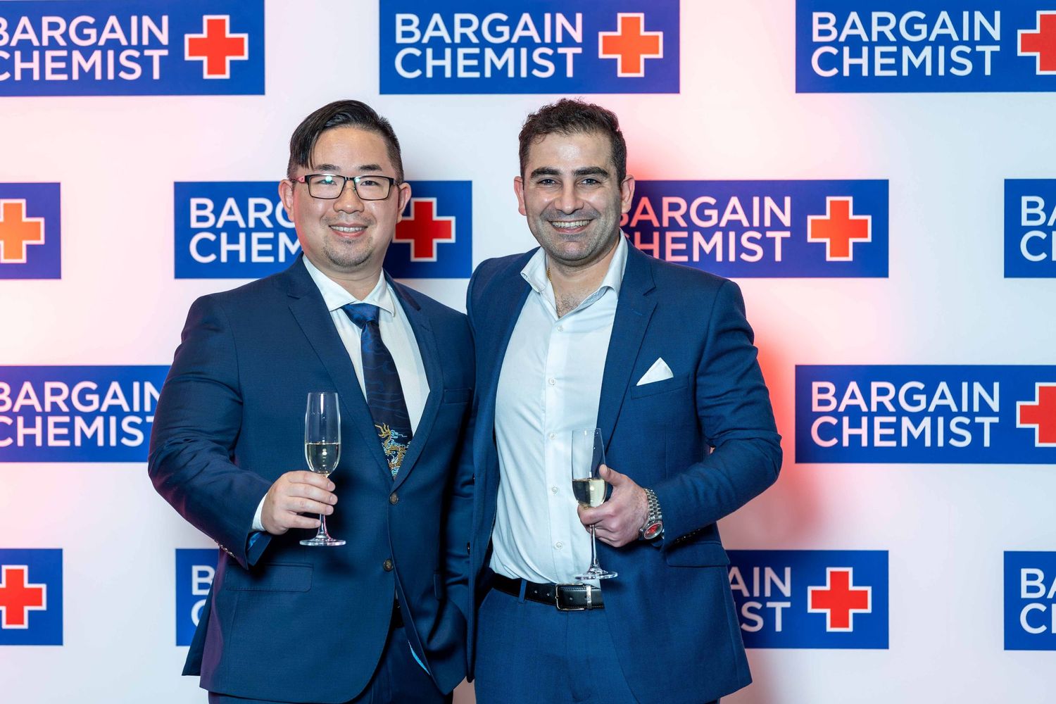 Corporate group photo with Bargain Chemist logo wall backdrop at business event.