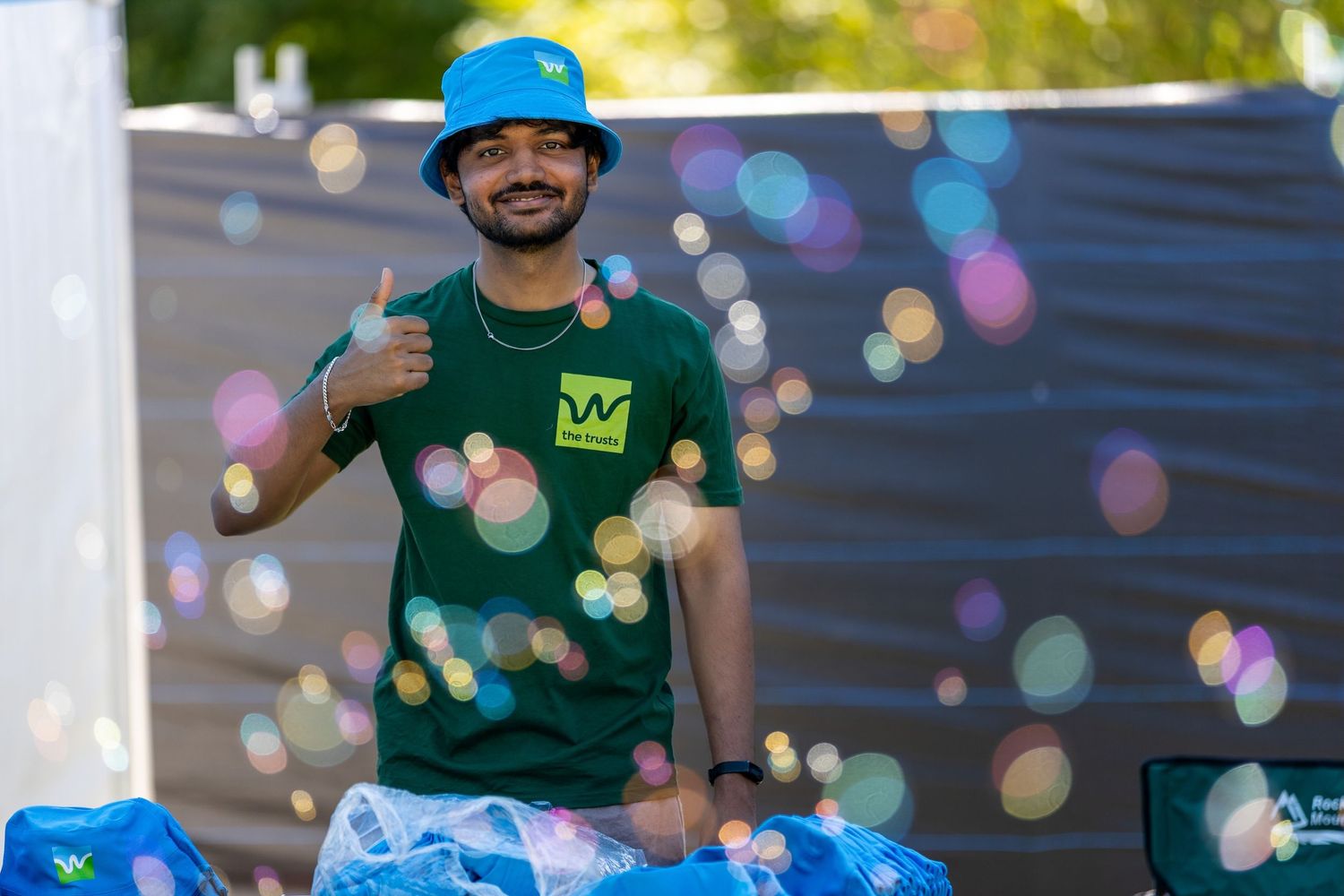 Staff members in green shirts and blue hats at outdoor event with colorful bokeh lighting.