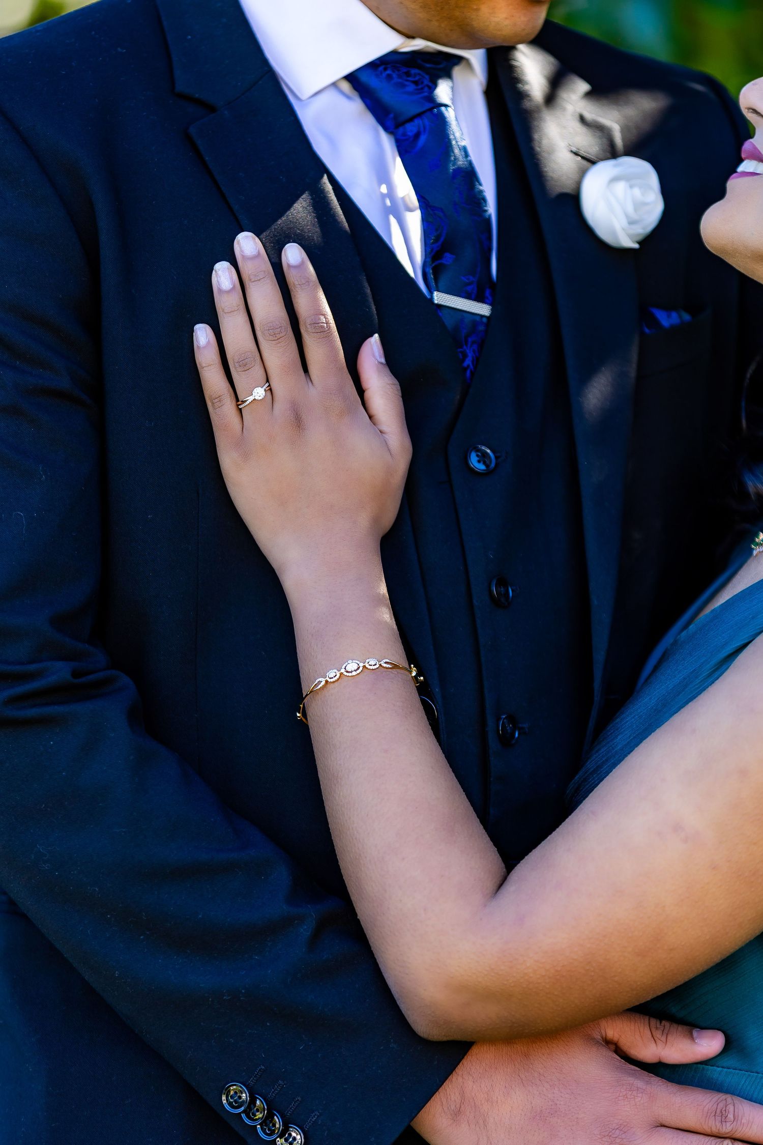 Close-up of a bride's hand with gold ring and bracelet resting on groom's navy blue suit at wedding.