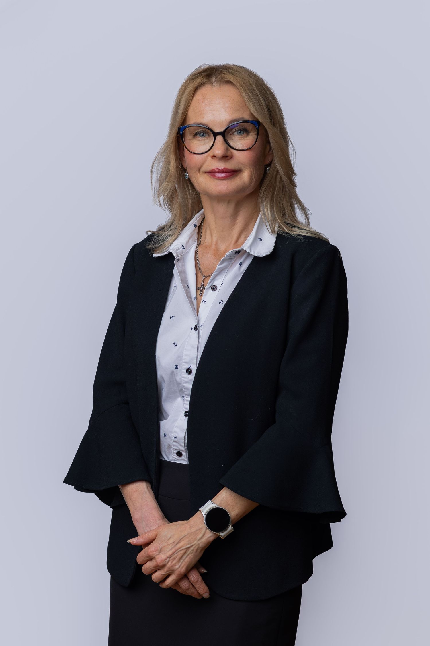 Professional woman in black blazer and glasses poses confidently against a light gray background.