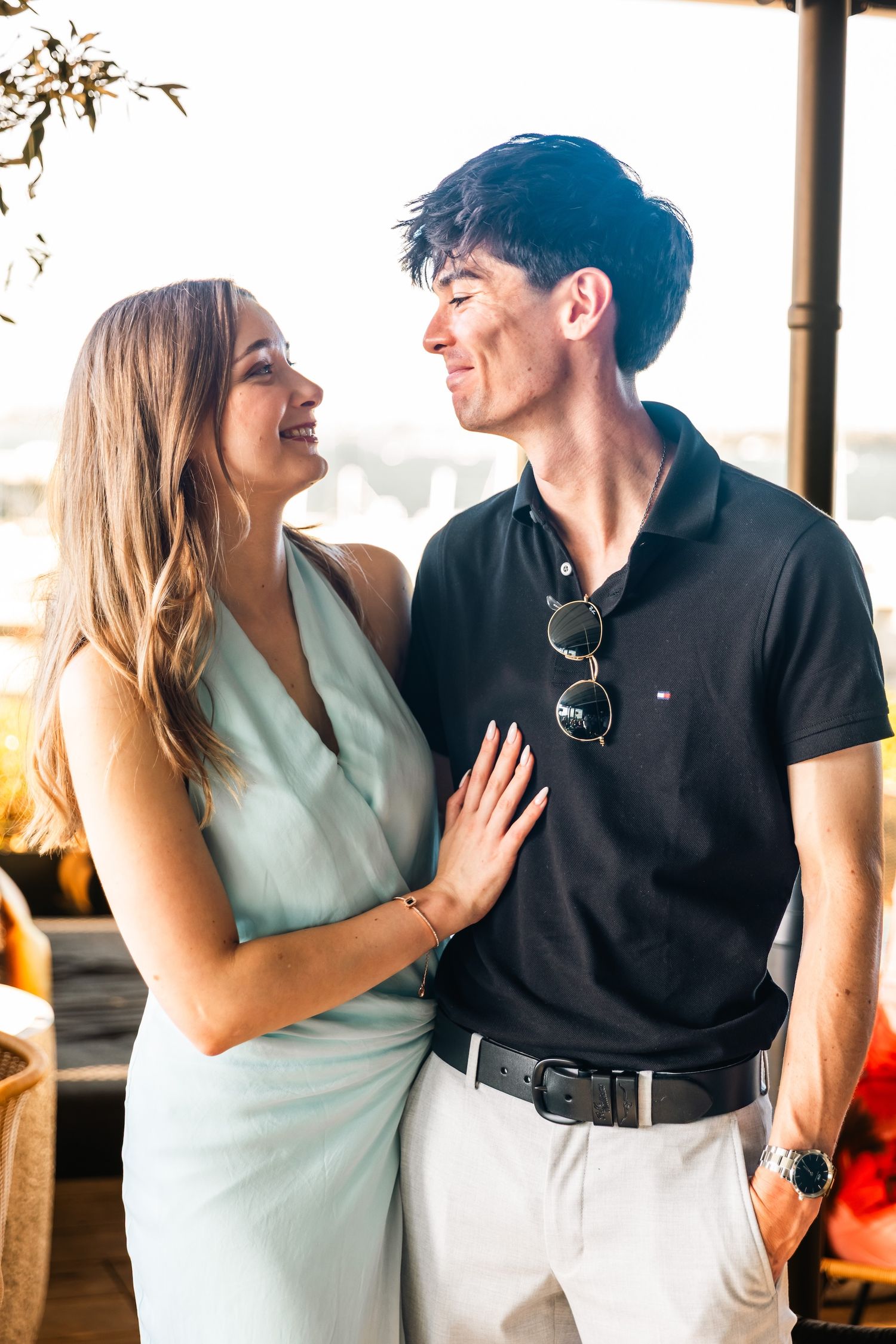 A smiling couple in summer attire gazing at each other on a sunny outdoor terrace.