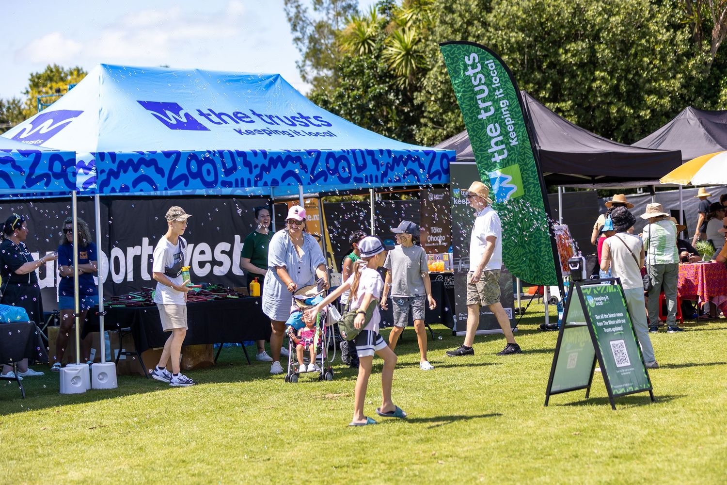 Sunny outdoor festival scene with white tents and scattered attendees on grassy field.
