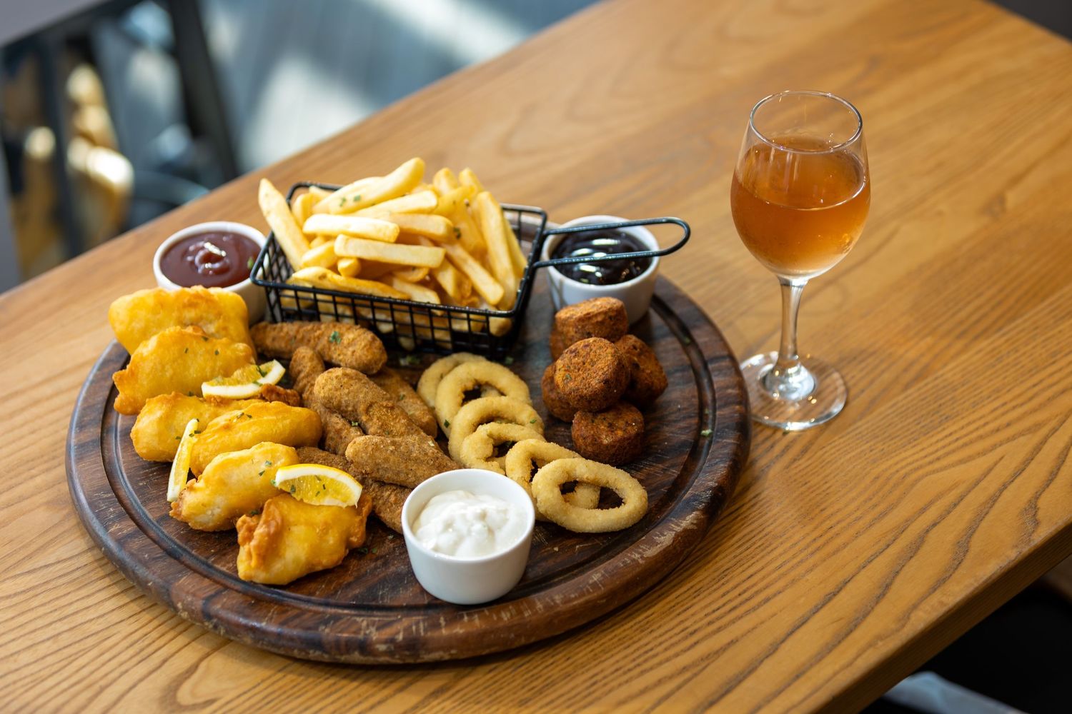 Crispy fried fish and french fries arranged on wooden serving boards with beer glasses.