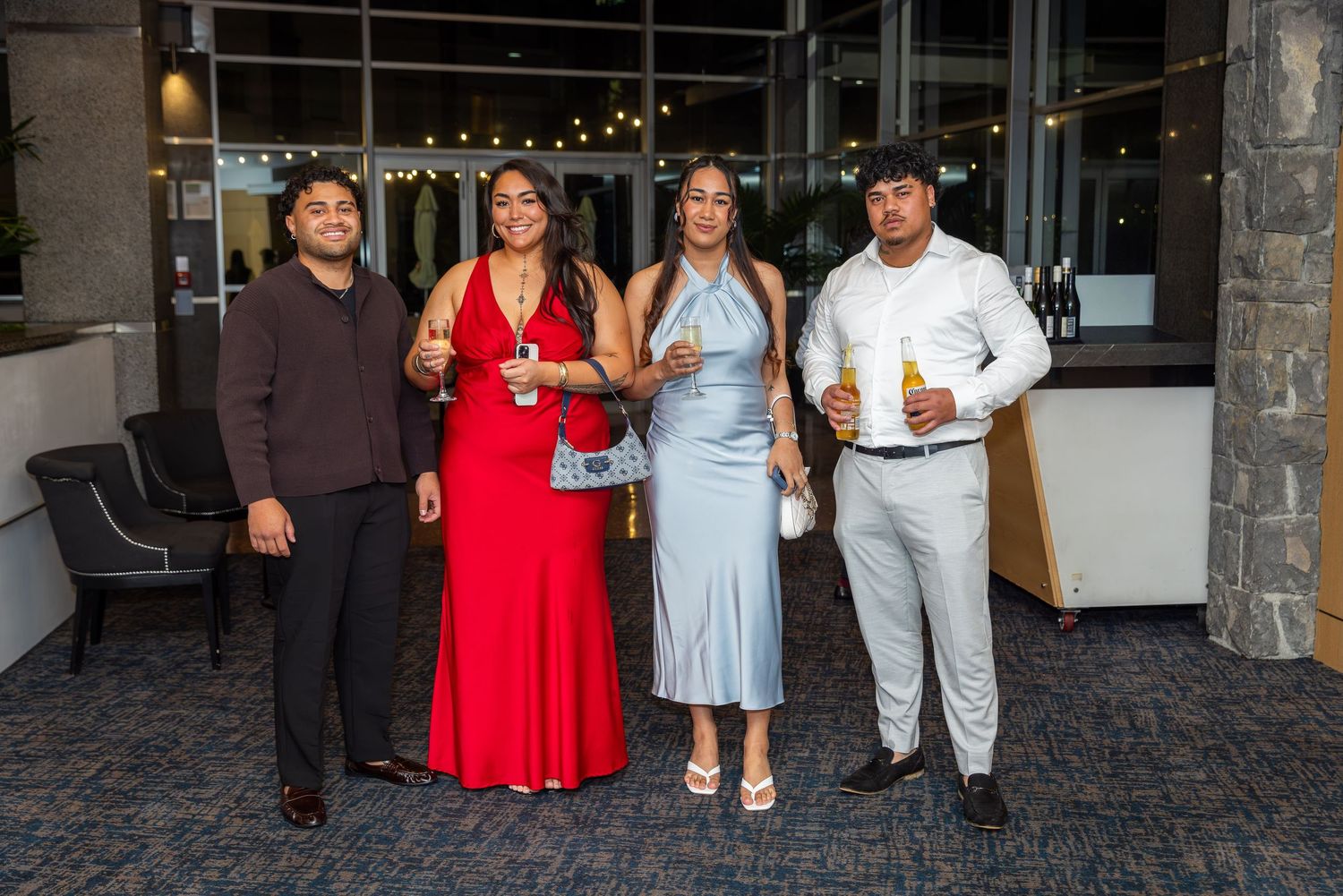 Four elegantly dressed friends posing together at a formal event, wearing red, silver, and white outfits.