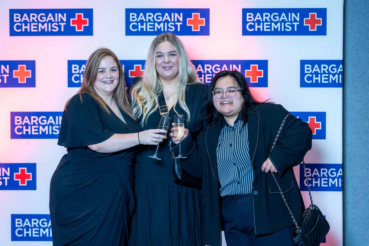 Attendees posing for photos at Bargain Chemist event with branded backdrop.