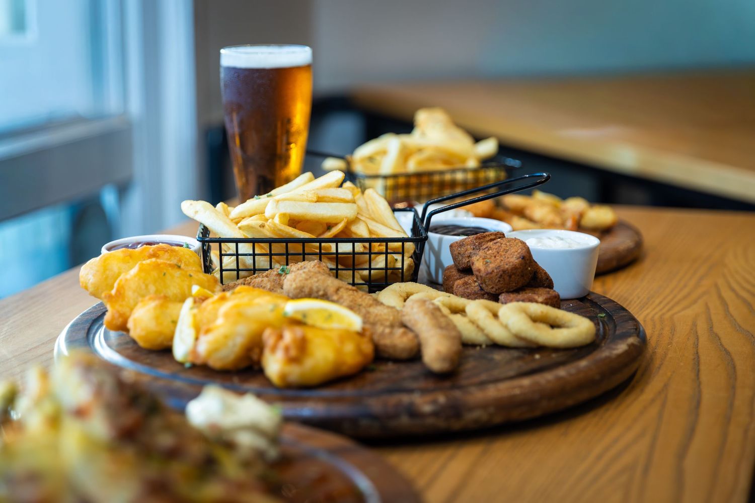 Bar food spread including fried appetizers and craft beers on rustic wooden serving boards.