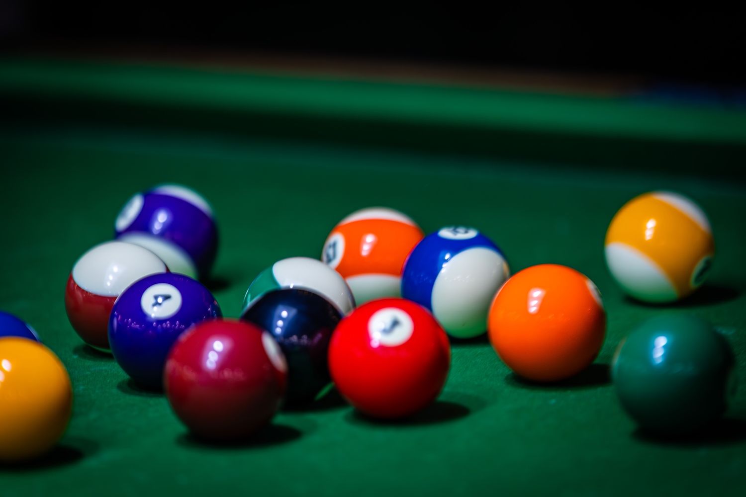 Colorful pool balls scattered on green felt billiards table with shallow depth of field.