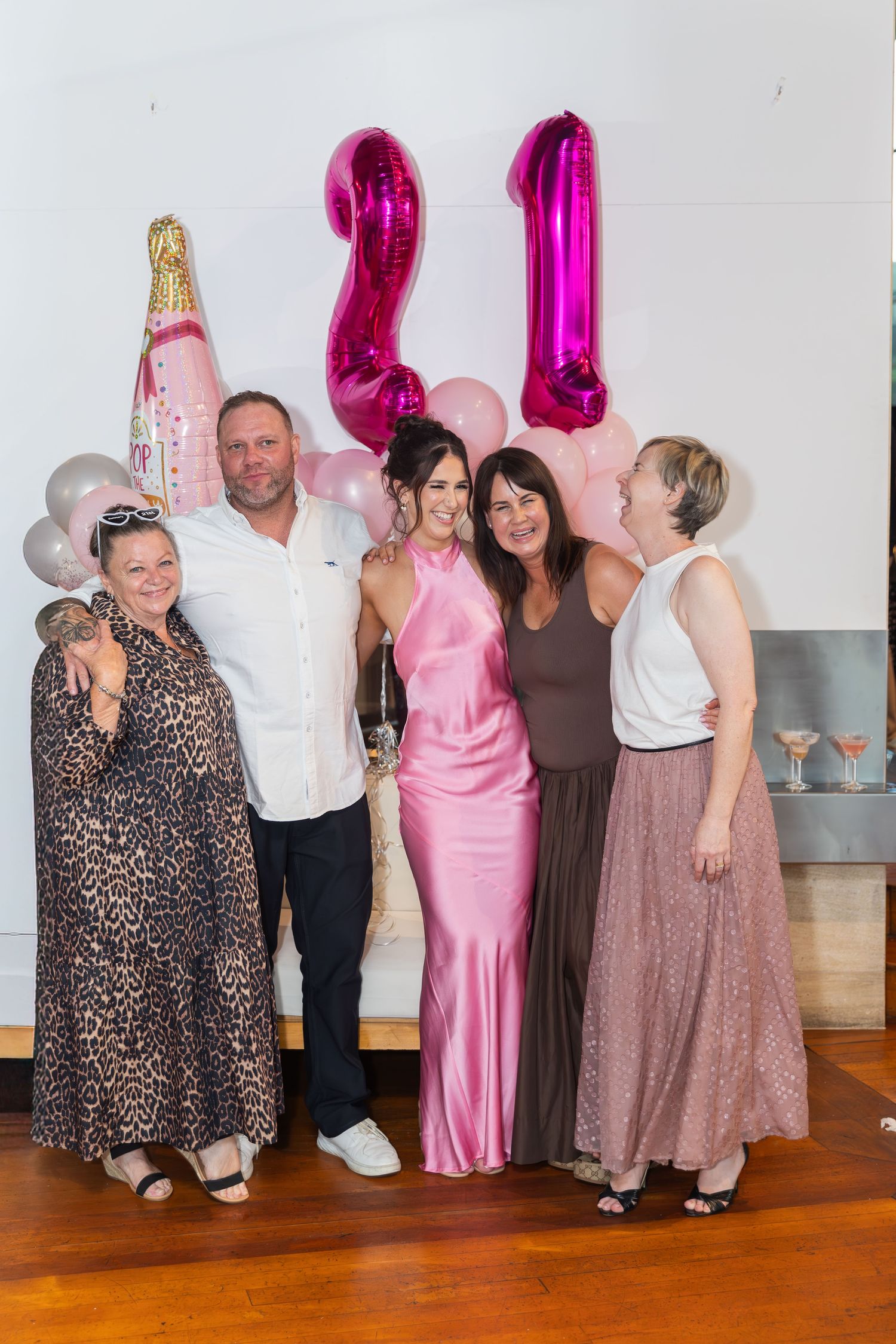 Group of five people posing at a 21st birthday party with pink number balloons and champagne bottle balloon.