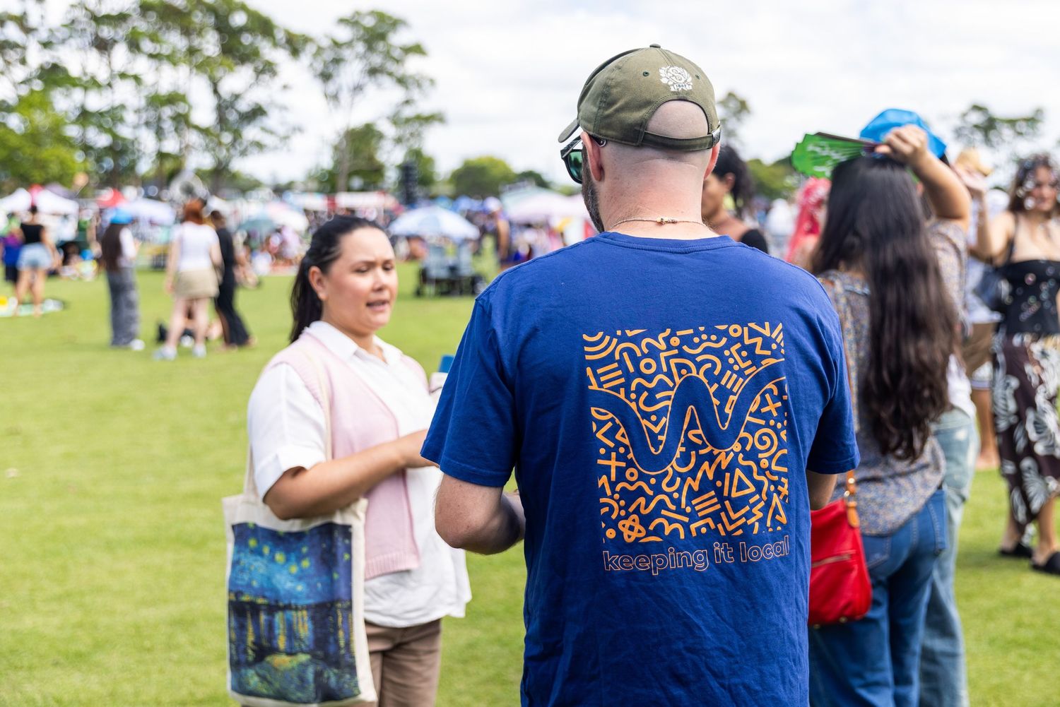 Crowd gathering at an outdoor event with merchandise displays visible.