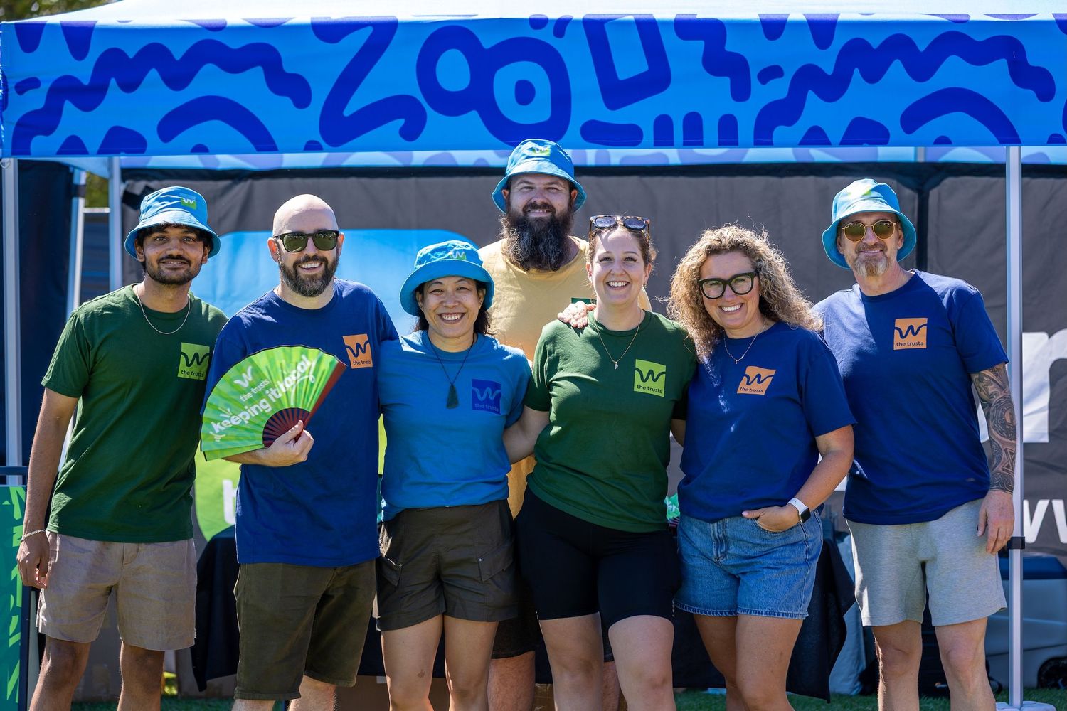 Team members in blue and green uniforms posing together at outdoor event.