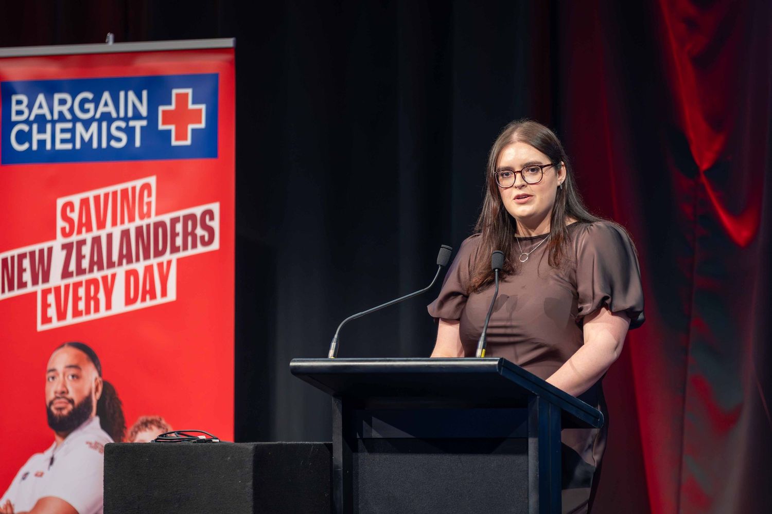 Conference stage setup with Bargain Chemist logos and red promotional banners.