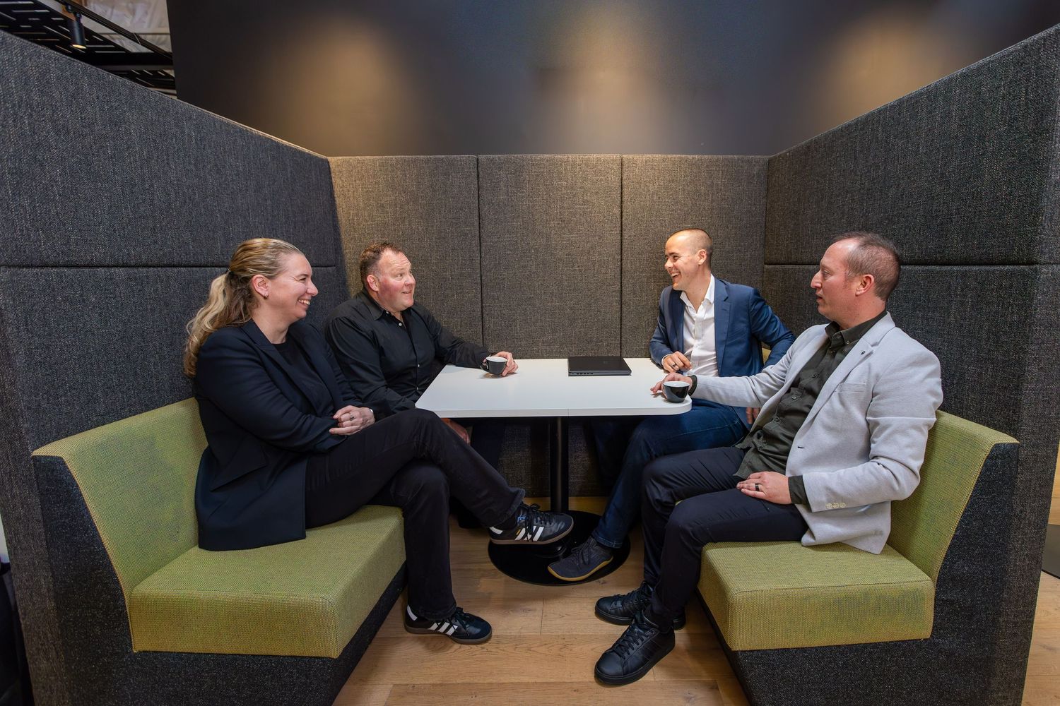 Four business professionals having a meeting in a modern office booth with green sofas and a white table.