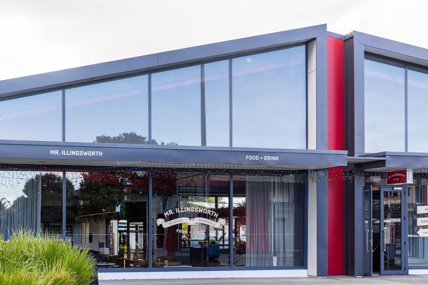 Modern commercial building exterior with glass windows and red accents stretches across multiple connected storefronts.