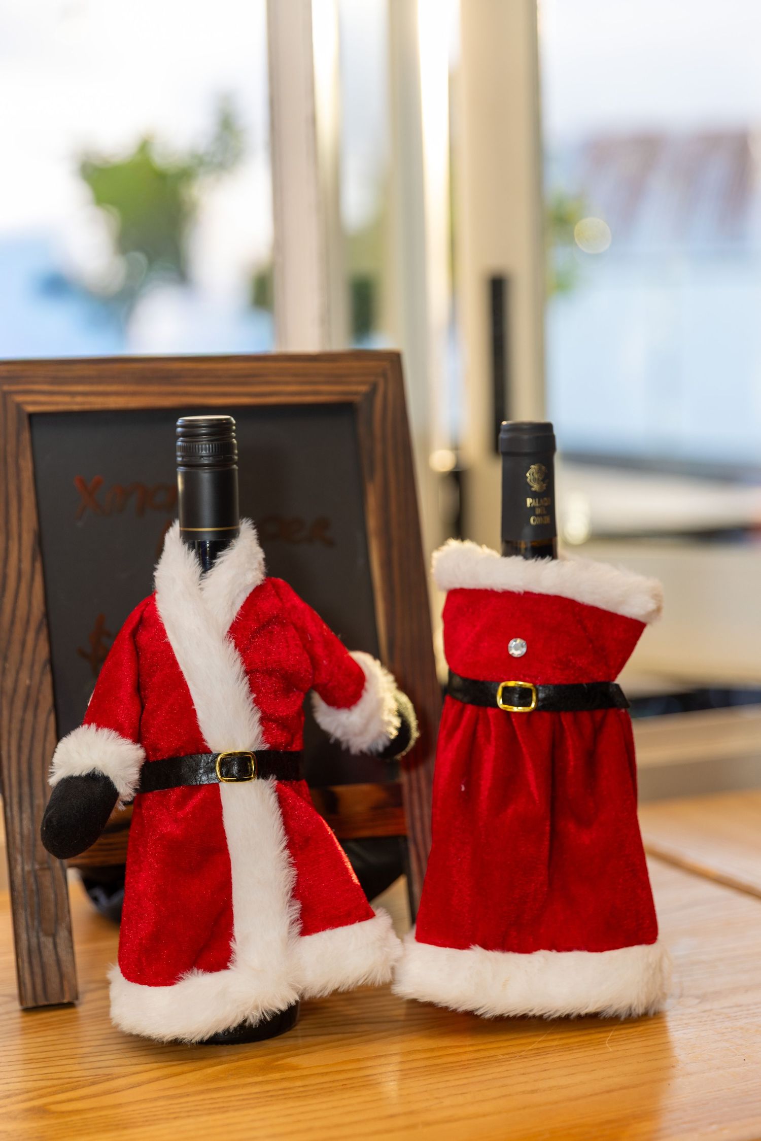 Wine bottles decorated with festive Santa hat covers displayed on wooden table.