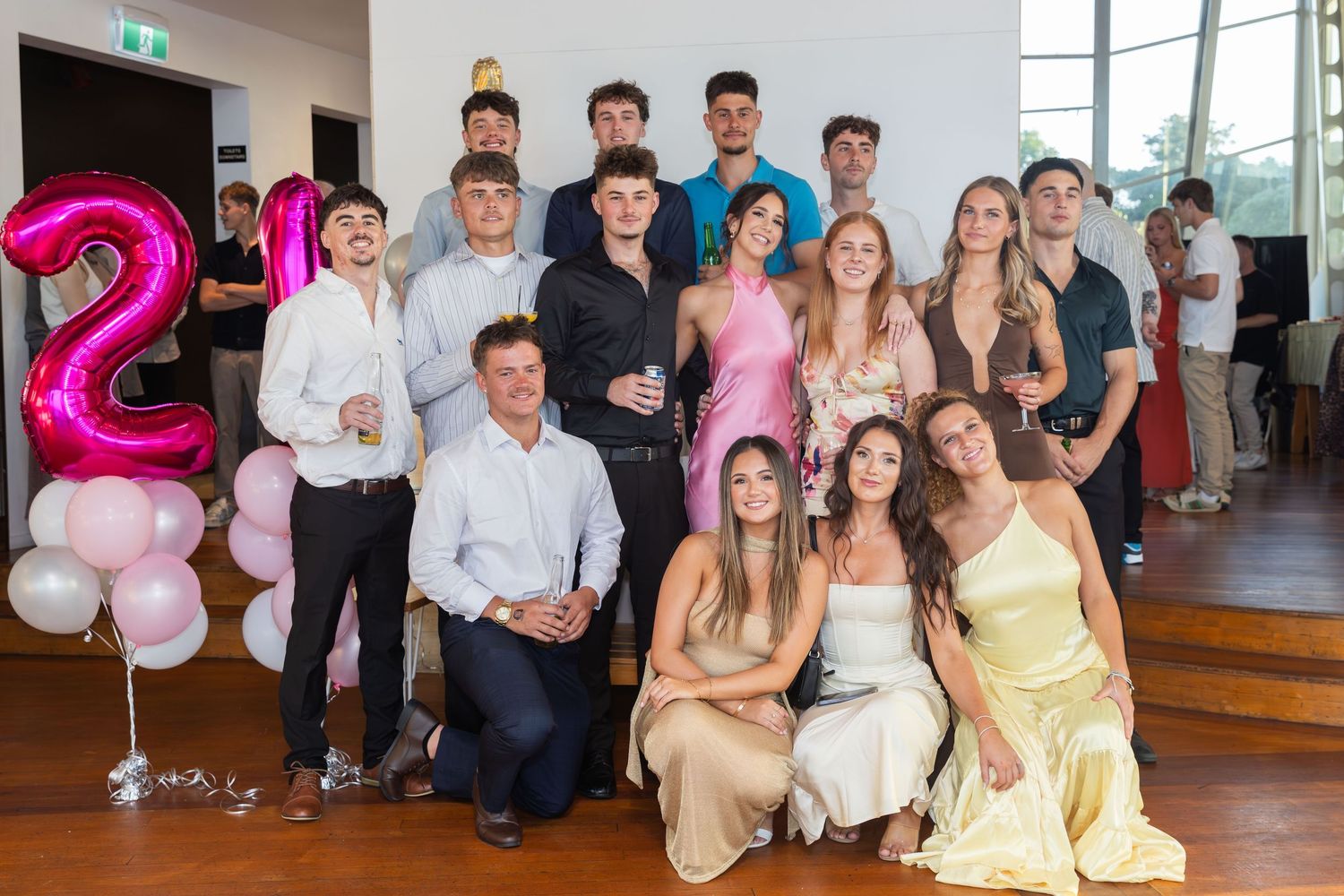 Group of young adults posing together at a 21st birthday party celebration with pink balloon decorations.