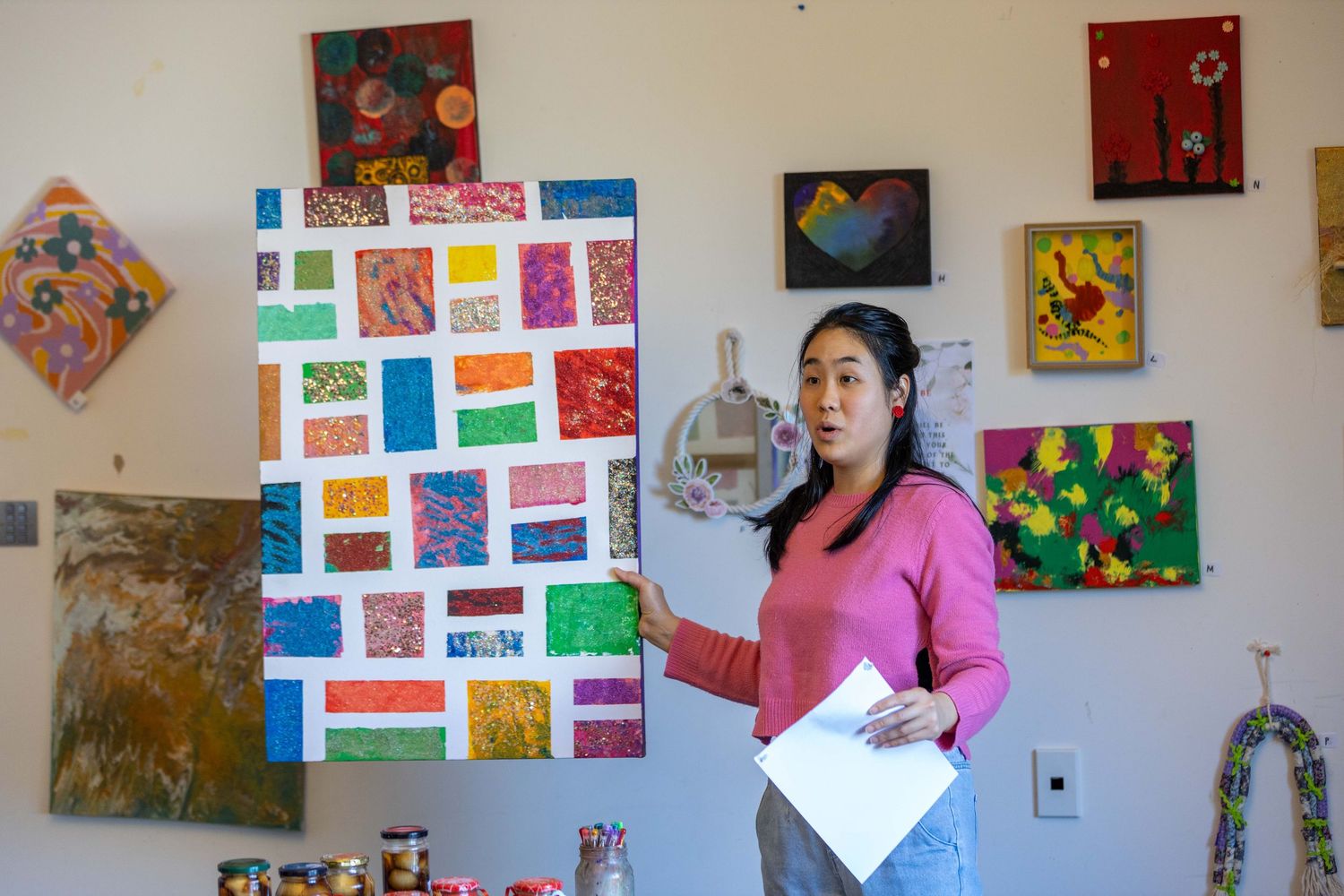Artist presenting colorful abstract collage artwork in a studio gallery with multiple paintings displayed on white walls.