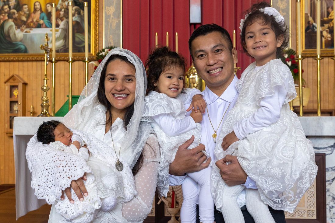 Family dressed in white celebrating a baptism ceremony inside a decorated Catholic church.