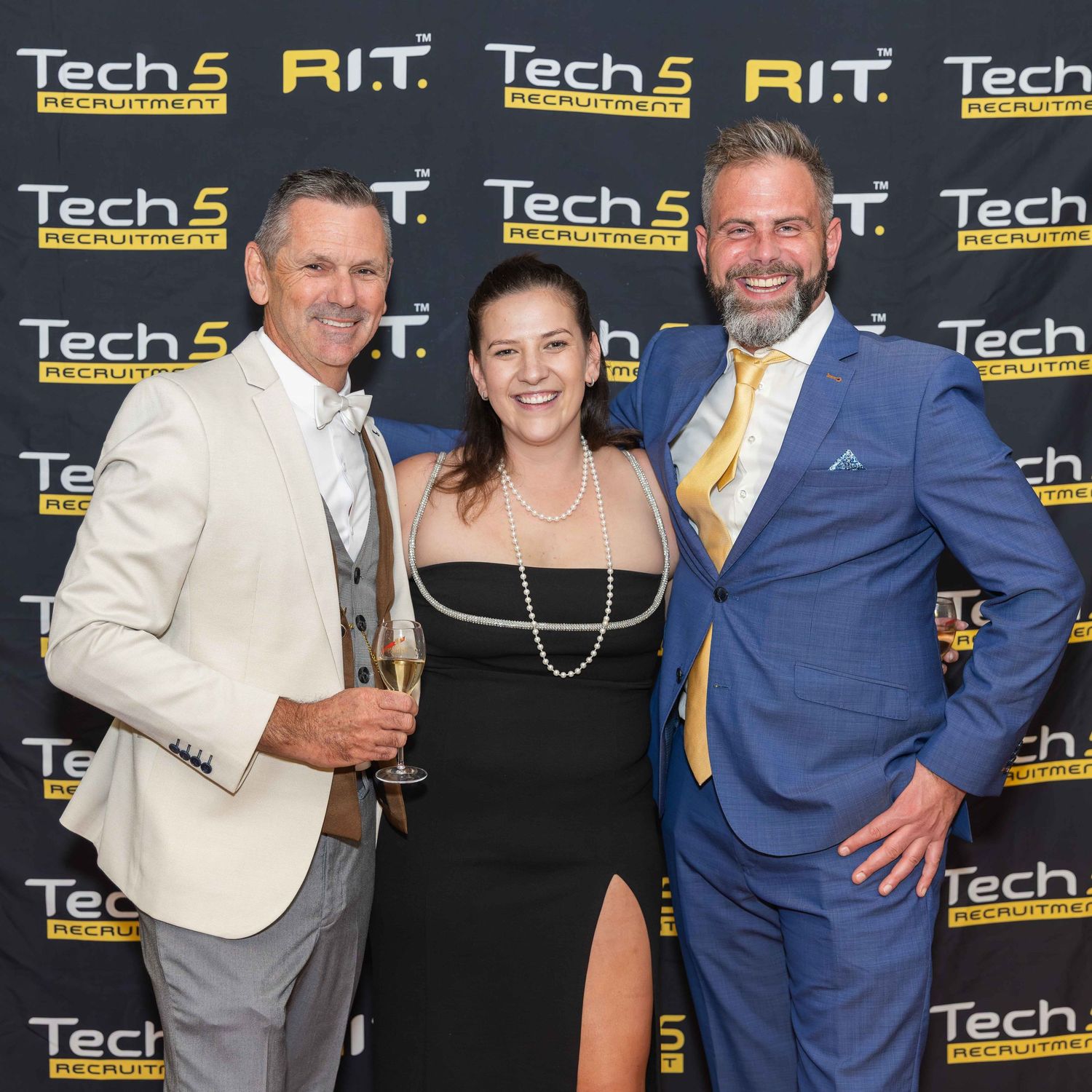 Three professionals posing at a Tech5 Recruitment and RIT event, dressed in formal attire at a branded backdrop.
