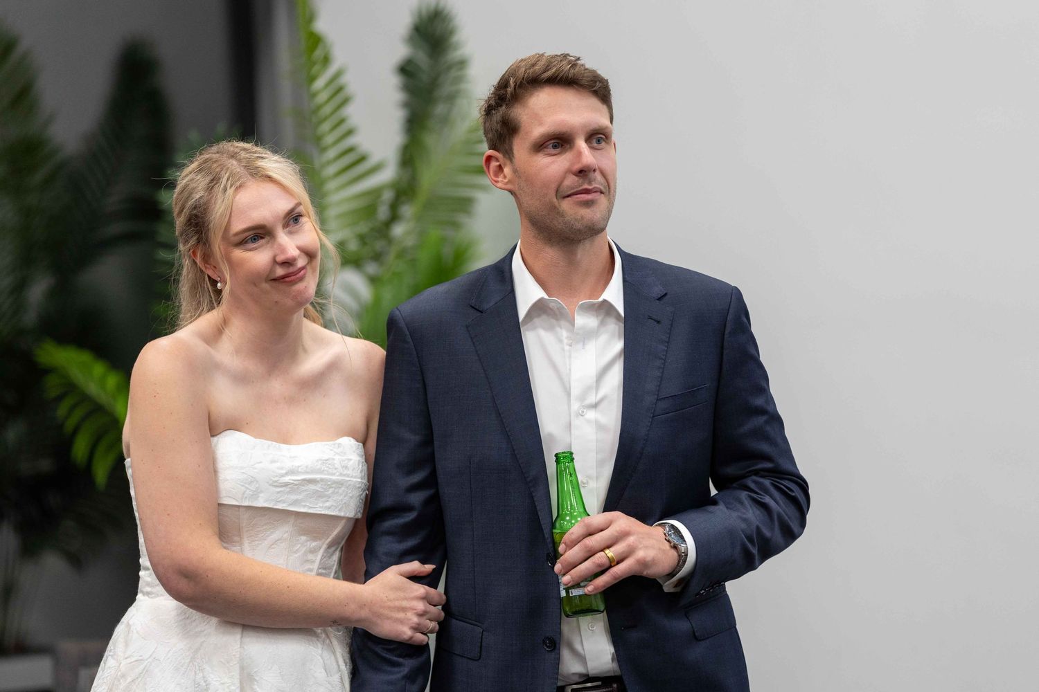 Bride in white dress and groom in navy suit share drinks during wedding celebration.