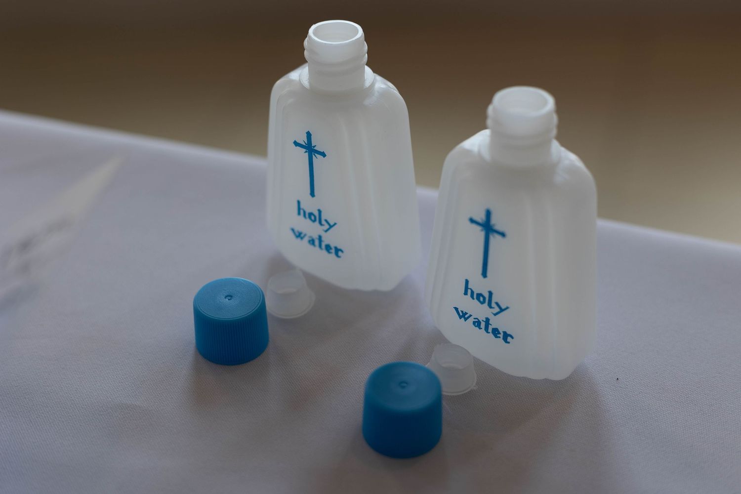 Two small plastic holy water bottles with blue crosses and caps on a white surface.