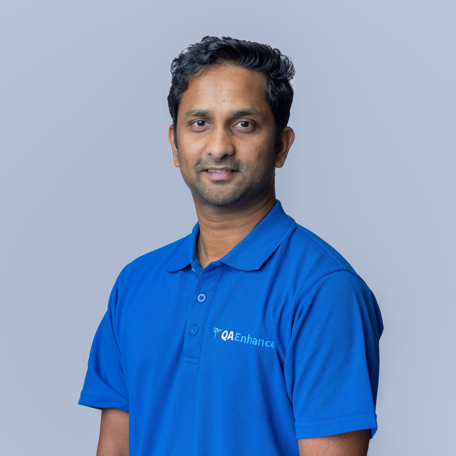 Professional man in blue QA Enhance polo shirt poses confidently against a gray background.