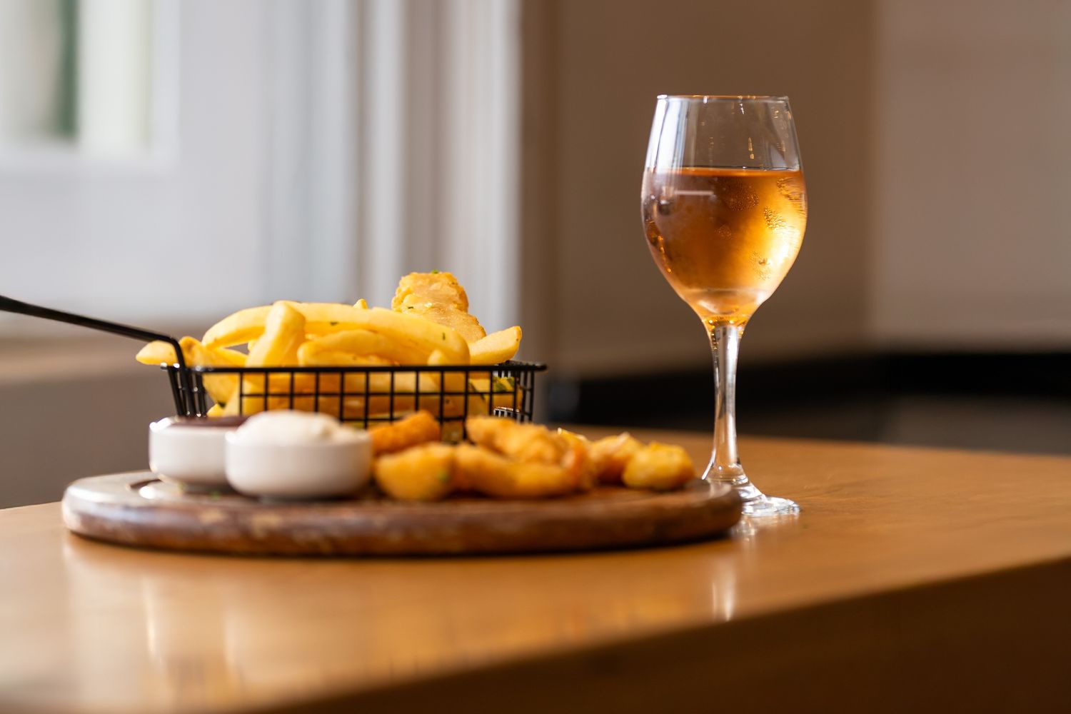 A glass of golden beer sits on a wooden table next to sliced oranges and white foam garnish.