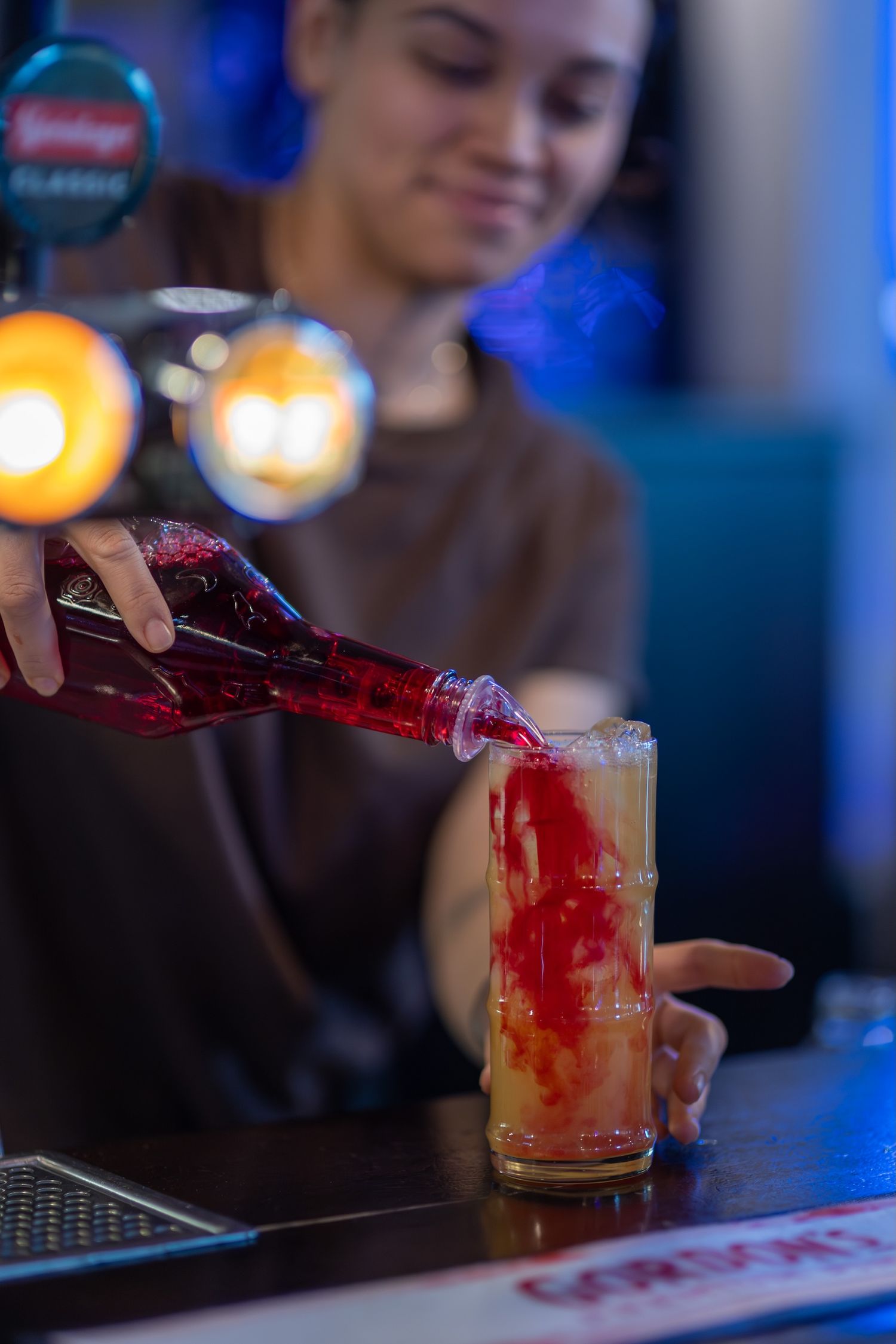 Bartender pouring red cocktail mixer into glasses with ice and garnish.