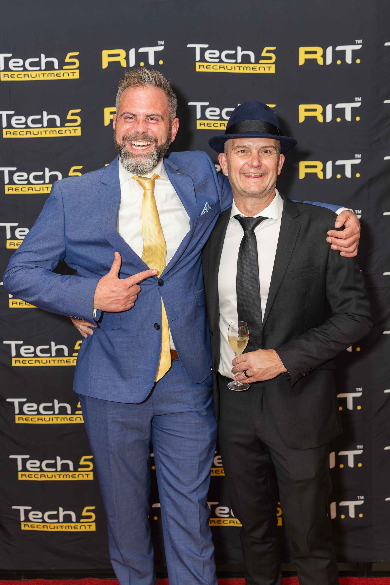 Two men in suits pose on a red carpet at a Tech5 Recruitment and R.I.T. event.