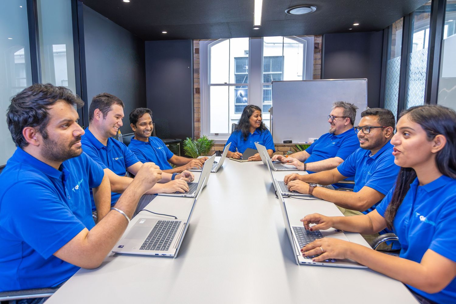 Team of professionals in blue shirts collaborating in a modern conference room with laptops.