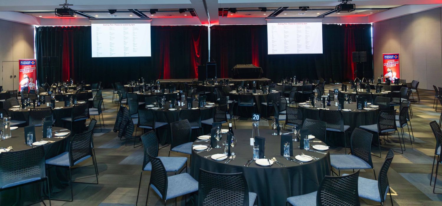 Panoramic view of an elegant event space with black tables and ambient red lighting.