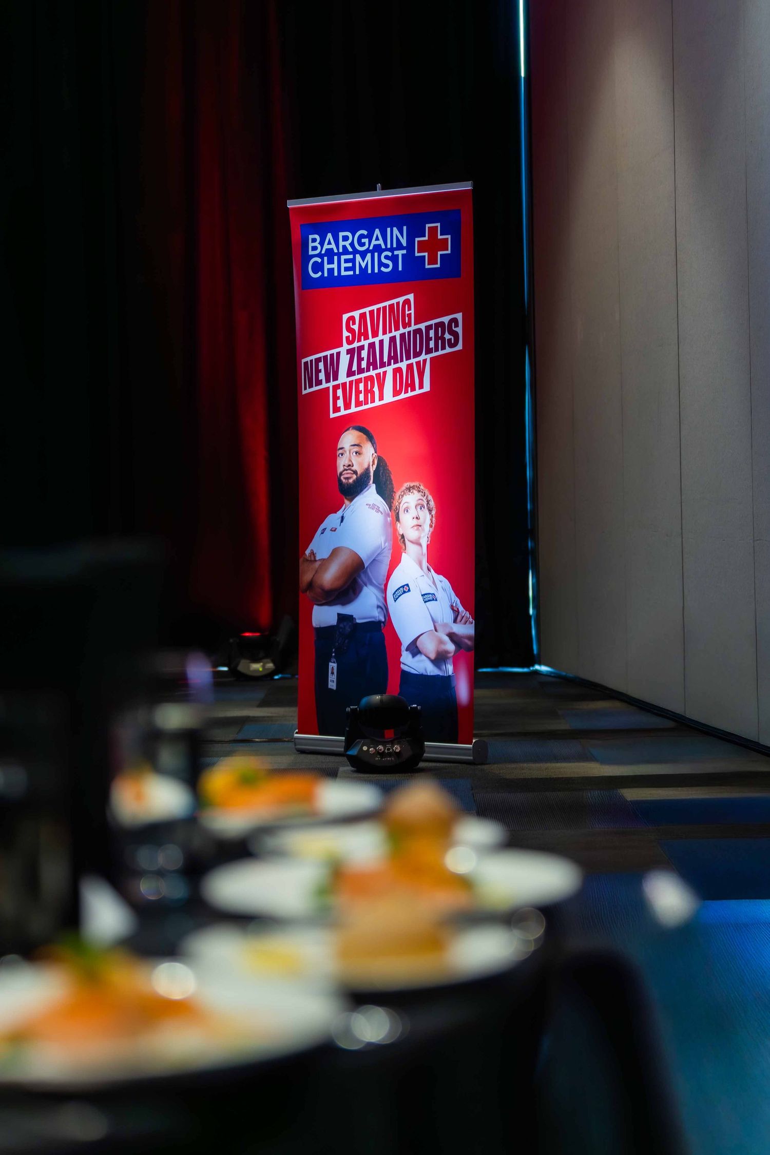 Red illuminated promotional displays at a corporate event with dining tables in the foreground.