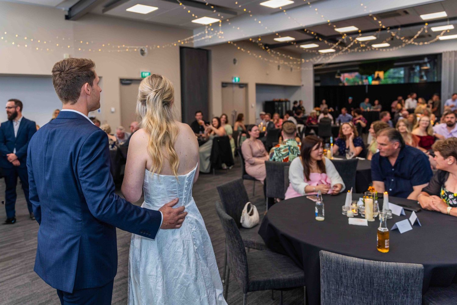 Wedding guests celebrate at reception tables in a modern venue.
