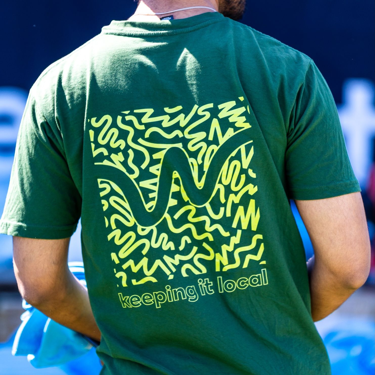 Green t-shirts with yellow abstract pattern designs displayed at an outdoor event.