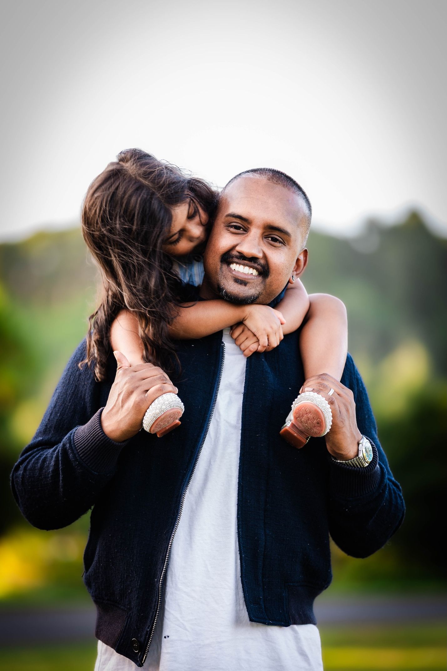 Smiling man giving a young girl a piggyback ride outdoors in a park setting.