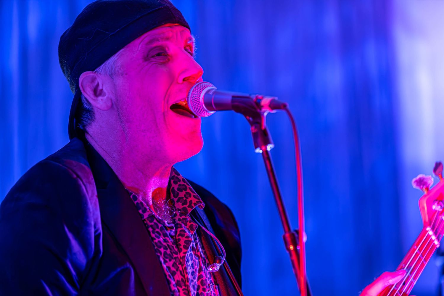 Male vocalist performing on stage under blue and purple lights, singing into a microphone at a live music event.
