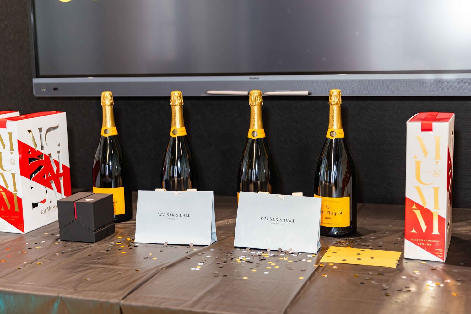 Four Veuve Clicquot champagne bottles displayed on a wooden table with branded gift boxes at an event.