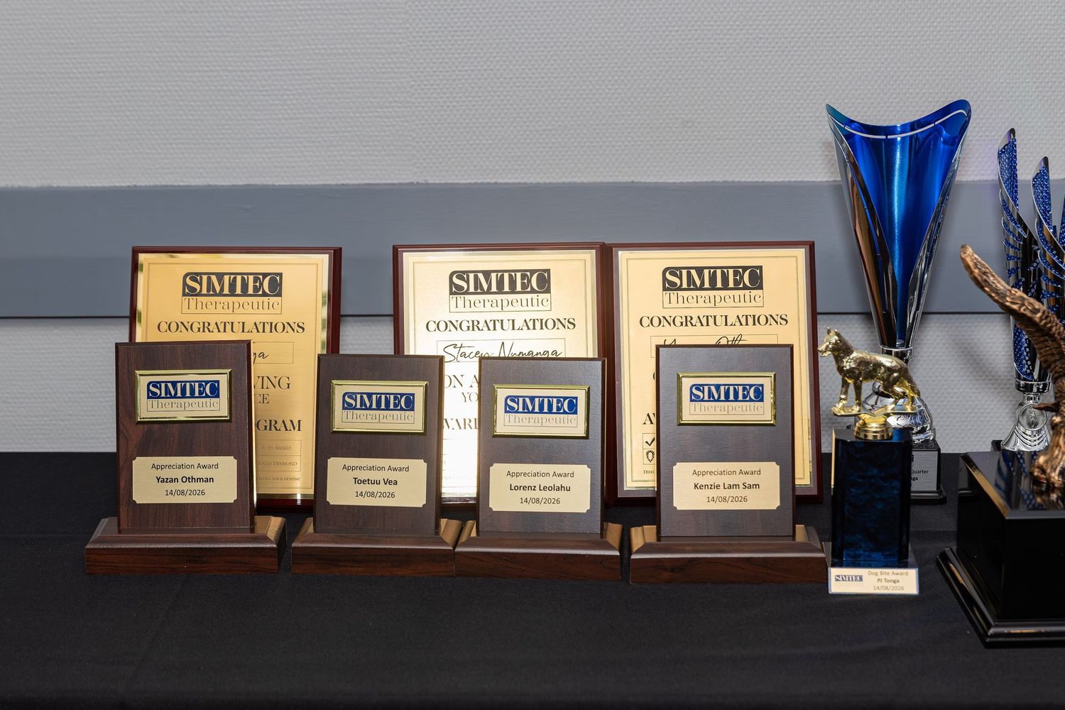 SIMTEC award plaques displayed on a table alongside a blue glass trophy at a recognition ceremony.